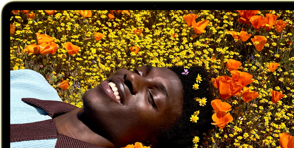 MacBook Neo, color cítrico, persona sonriente tumbada en un campo de flores en la pantalla